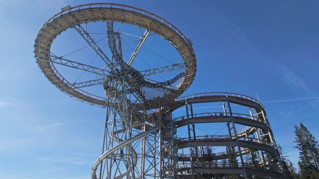 SkyWalk Serce Poronina observation tower in Male Ciche, Poland, with spiral ramp, slide and elevated walkway above forest trees on a sunny day in the Tatra region.