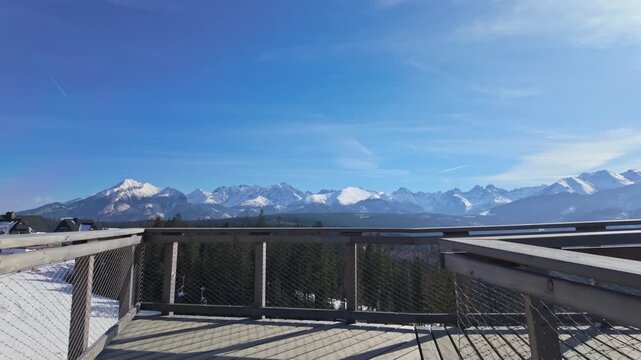 SkyWalk Serce Poronina in Male Ciche, Poland, observation deck overlooking the snowy Tatra Mountains above coniferous forest under a clear blue winter sky.