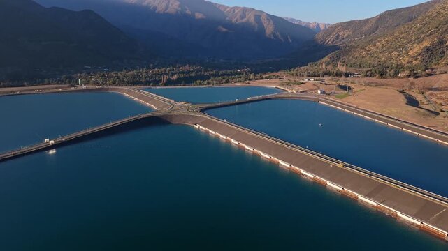 Forward flight approaching four geometric water treatment ponds arranged in a cross pattern beside a small rural mountain town bathed in warm golden evening sunlight