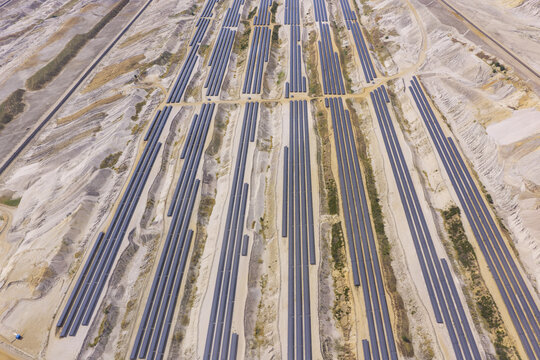 Aerial view of a large solar farm installed within an open-pit brown coal mine with rows of photovoltaic panels arranged on sandy terrain in Germany.