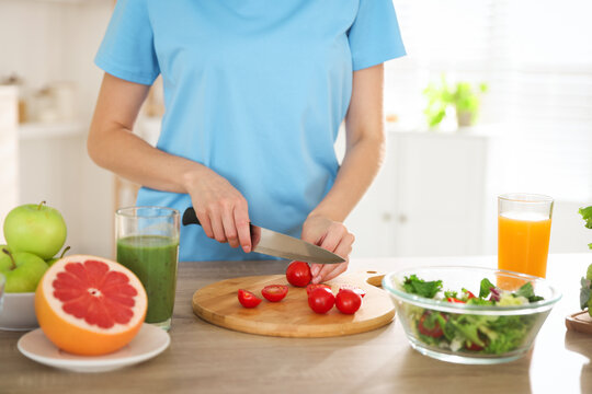 Healthy diet. Woman cutting tomatoes for salad at wooden table indoors, closeup