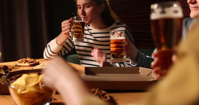 Friends clinking glasses of beer at table indoors, camera moving in
