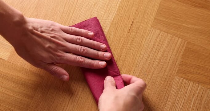Man folding red napkin at wooden table indoors, above view. Camera moving in and out