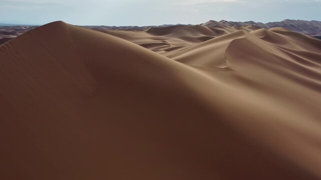 Aerial view of the vast sand dunes of the Gobi Desert with rolling ridges and shadows under a clear sky in Mongolia.
