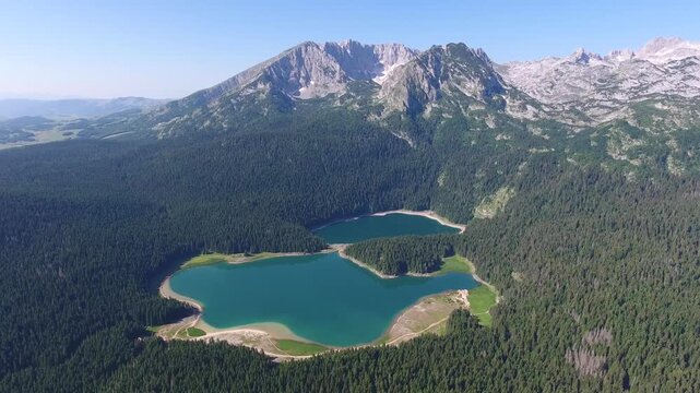 Aerial view of Black Lake surrounded by dense pine forests with the peak of Bobotov Kuk in the background in Zabljak Municipality, Montenegro.