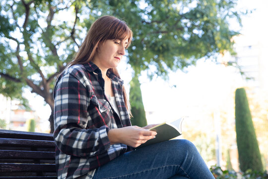 young woman reading a book on a city park bench