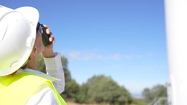 Woman in a hard hat inspecting a wind turbine while using a two way radio to communicate
