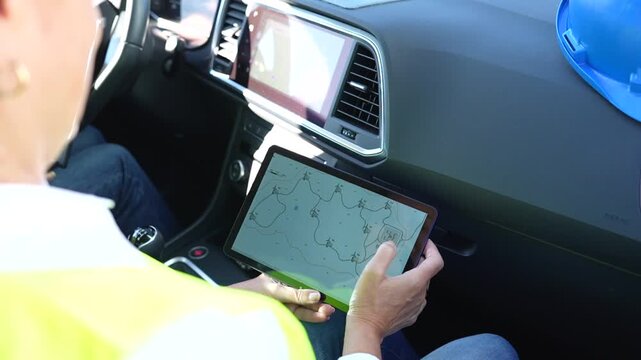 Engineer inside a car using a tablet to check the map of a wind turbine power plant