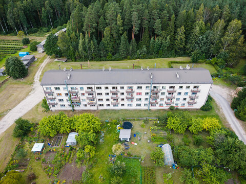 Aerial view of a residential apartment building surrounded by small vegetable gardens, greenhouses, and lush green trees in Lielsalas, Talsi Municipality, Latvia.