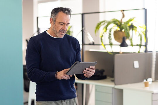 Man holding tablet, standing in office near turquoise partition with coffee cup, copy space