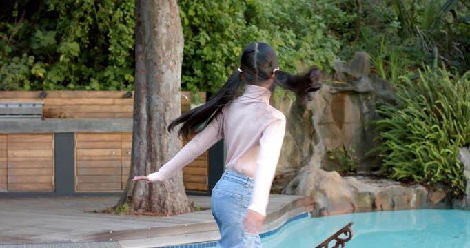 Indian girl child stepping onto wooden deck beside swimming pool, spinning with pigtails flaring