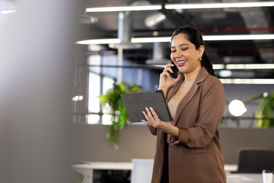 Professional woman using tablet and smartphone near workstation in open-plan office, copy space