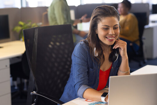 Diverse coworkers collaborating around laptop at shared office desk with printed charts, copy space