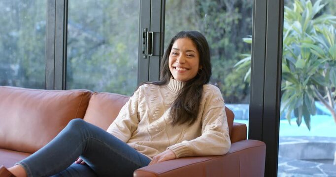 Smiling at camera opening discussion, woman tucking hair, gesturing on sofa by sliding glass door