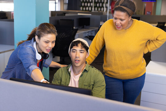 Diverse coworkers collaborating at computer monitor in open office with headphones