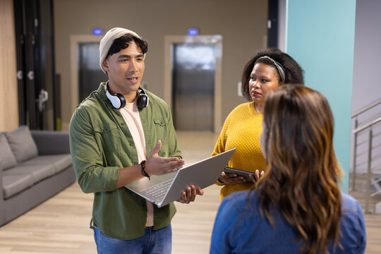 Diverse coworkers standing in office lounge presenting project with laptop, tablet and headphones