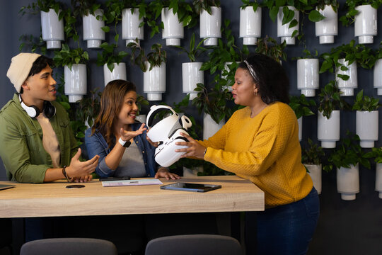 Diverse coworkers examining white VR headset while reviewing tablet and documents at office