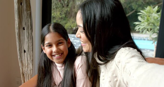 Mother and Indian schoolgirl daughter raising smartphone for selfie, sharing smiles and tongues