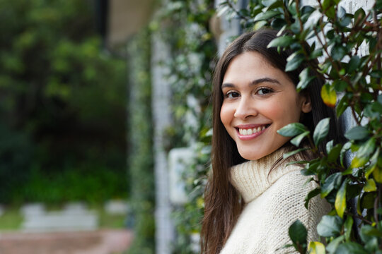 Woman leaning on vine-covered wall in garden beside stone path wearing knitted sweater, copy space