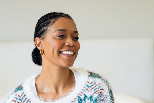 Mid adult woman sitting on bed smiling and looking right in soft fluffy knit sweater