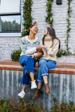 Female friends sitting on brick ledge outside white house wearing festive headbands and smartwatch