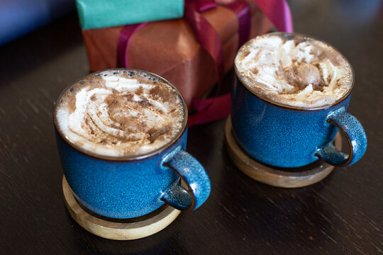 Two blue speckled mugs are resting on dark wooden table with whipped cream, Christmas gift