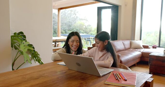 Mother and Indian girl pointing at laptop screen guiding drawing at dining table sharing high five