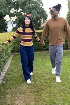 Couple holding hands and walking along park path wearing Christmas headband, green glasses