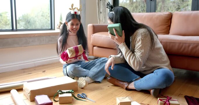 Picking pink ribbon, Indian girl child and mother wrapping holiday gifts using kraft paper at home