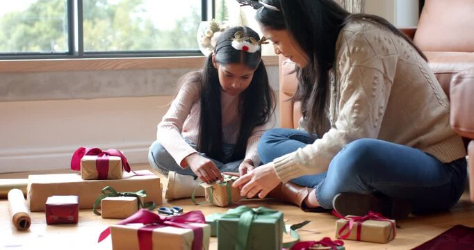 Mother guiding Indian daughter threading gift ribbon while wrapping for holiday hugging at home