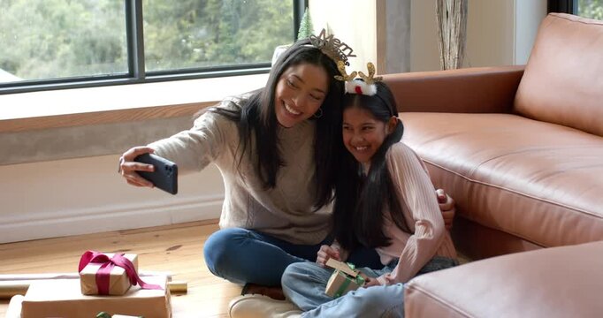 Mother and daughter unwrapping gift while posing with tiara antlers for selfie on hardwood floor