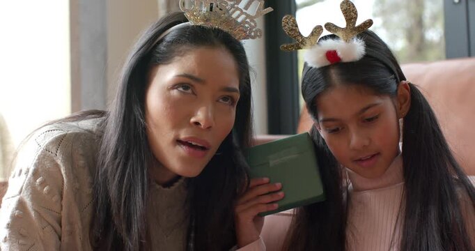 Indian mother and daughter examining gift box guessing contents wearing tiara and antlers on sofa