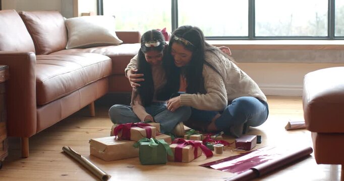 Child cutting ribbon sparking Asian mom and daughter wrapping boxes for gifting and hugging at home