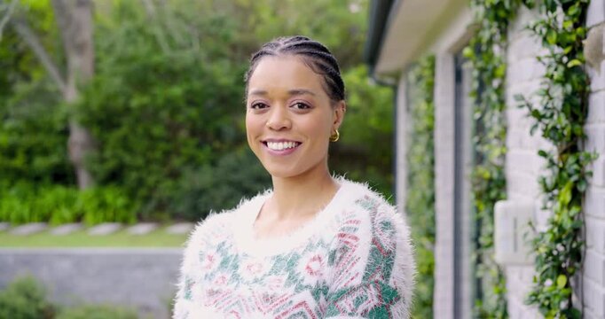Upon camera focusing, mid-adult woman smiling while modeling sweater hoop earrings in garden path