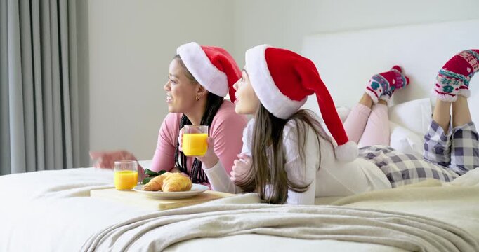 Diverse female pals in Santa hats sipping OJ pointing at window and eating croissants on Christmas