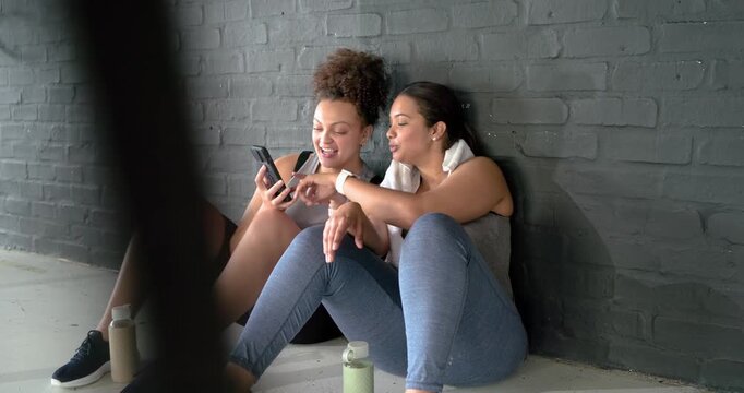 Holding smartphone Diverse female friends browsing feed, shifting phone, posing for selfie in gym