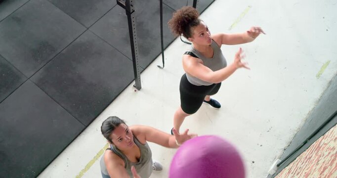 Wall target guiding diverse women squatting, launching medicine balls, catching rebounds at gym