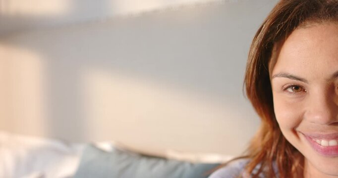 Sunlight drawing woman on sofa with pillow shifting gaze toward camera and smiling, copy space
