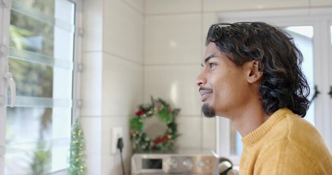 Adult man sensing camera presence turning head and smiling through blinds in kitchen with wreath