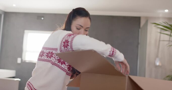 Female opening cardboard box, unpacking maroon Christmas sweater and placing pink quilt on bed