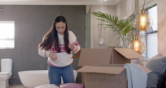 Adult woman wearing red knit folding packing clothes into box on bed marked Donations for Christmas