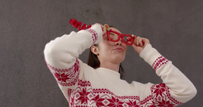 Adult woman putting on red glasses after puckering lips, adjusting headband in studio for Christmas