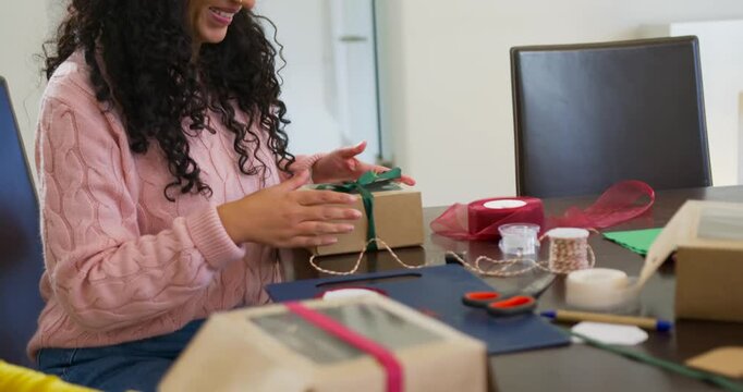 Diverse pink sweater women smiling tying ribbon wrapping boxes for Christmas at table, copy space