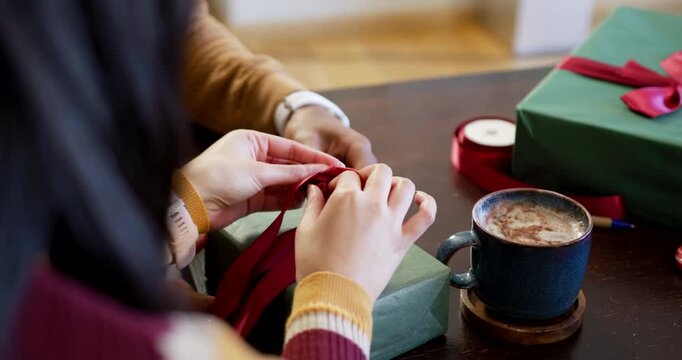After arranging red ribbon loops, two hands are tying Christmas gift bow at wooden table
