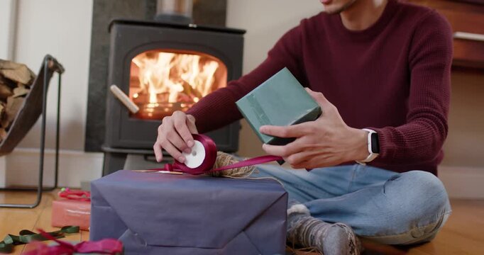 African American man preparing for Christmas by stove pulling ribbon and tying bow on gift
