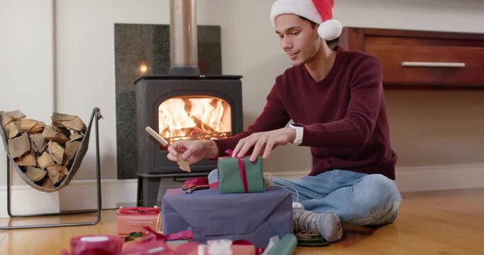 African American man in Santa hat wrapping green box atop parcel by stove, preparing for Christmas