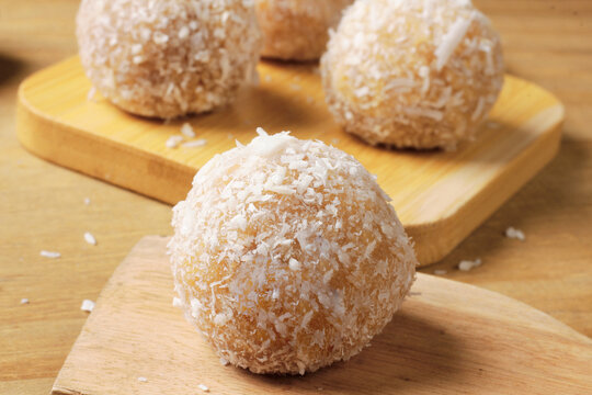 Handmade Brazilian round coconut beijinho coated in grated coconut, resting on a rustic wooden board. A traditional party dessert