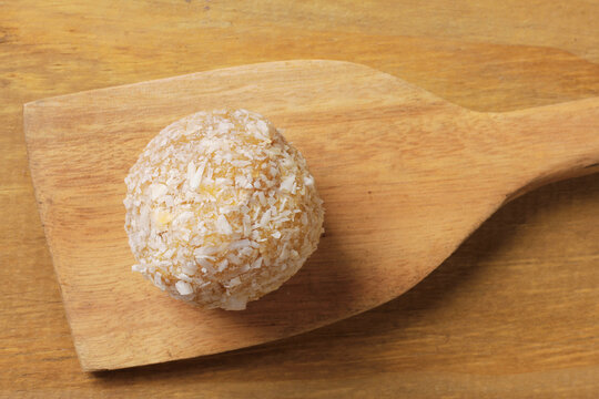 Brazilian coconut beijinho on a wooden spatula on a rustic wooden table. Traditional confectionery for parties and celebrations