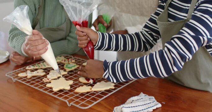 Decorating Christmas African-American family piping cookies in aprons using icing bags, copy space