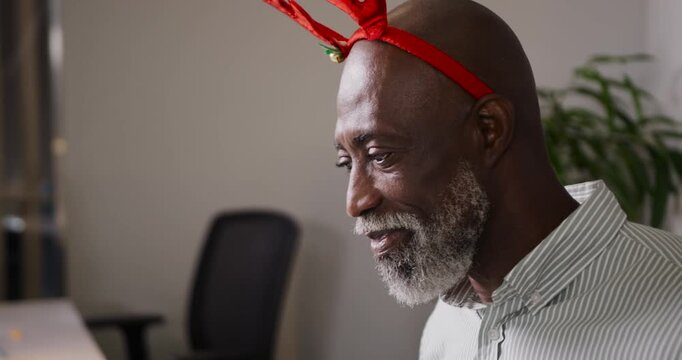 Senior man wearing red antler headband reacting and laughing at coworker off-frame during Christmas